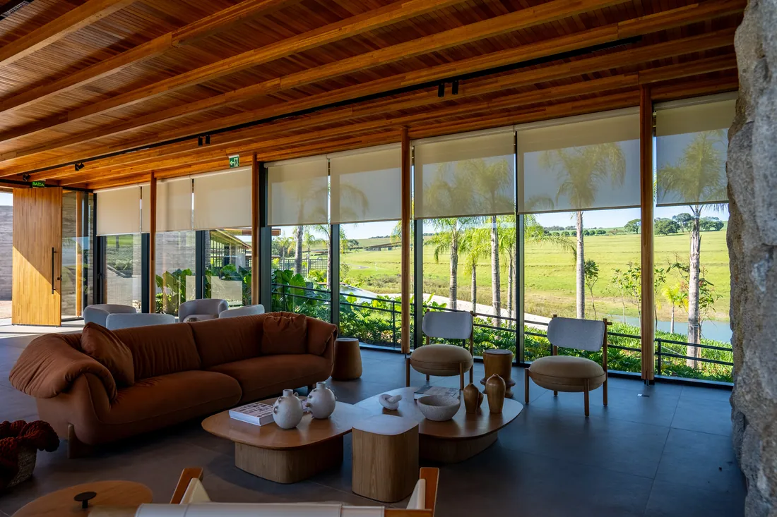 Lounge do clube com forro de madeira, sofás e vista para o gramado