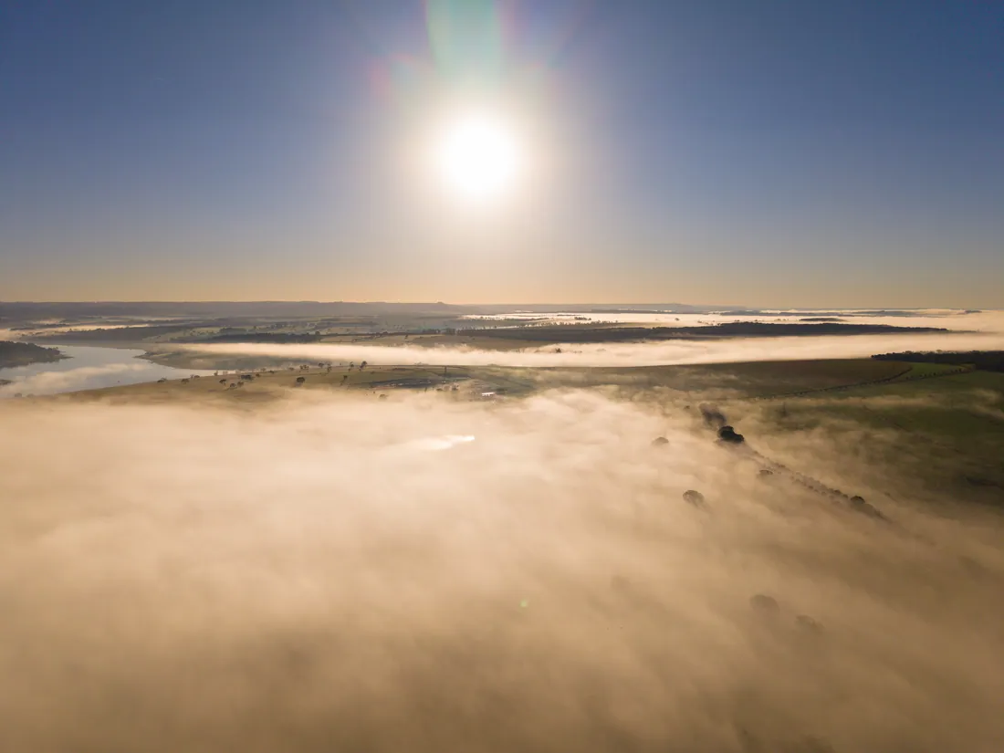 Vista aérea do Brisas coberto de neblina com o sol sobre a represa