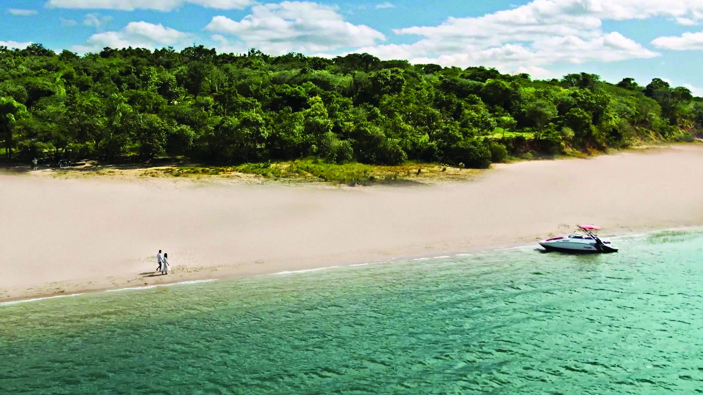 Lancha ancorada em uma praia de areia clara da represa, com a mata ao fundo